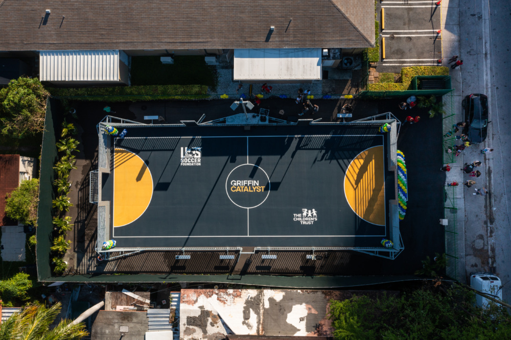 An aerial view of a navy blue and yellow mini-pitch that features logos of the U.S. Soccer Foundation, Griffin Catalyst, and The Children's Trust.